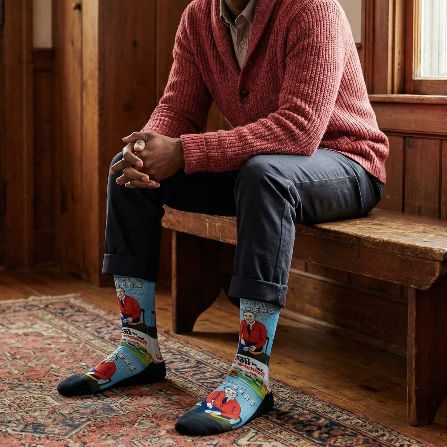 Man sitting on a wooden bench wearing a red sweater and colorful socks with a Mr Rogers Neighborhood pattern.