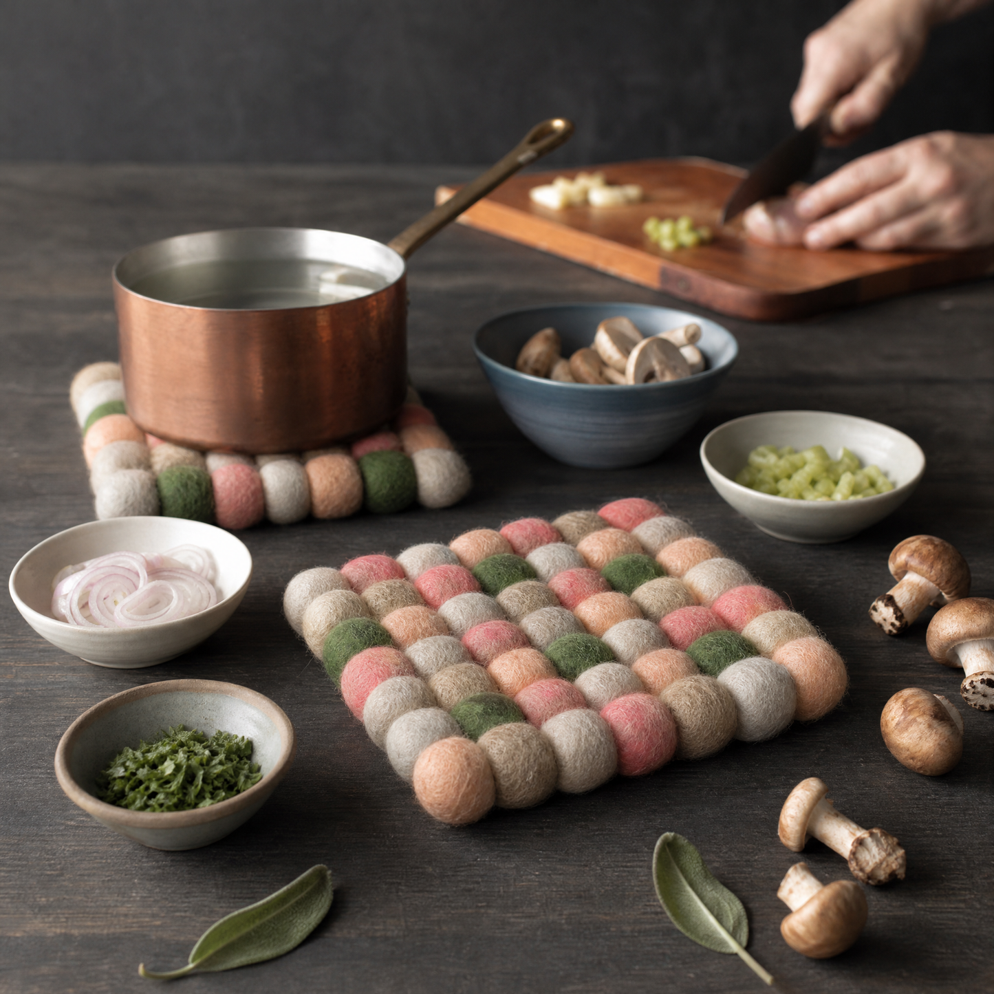 Colorful felt trivets on a dark surface with cooking ingredients and utensils.