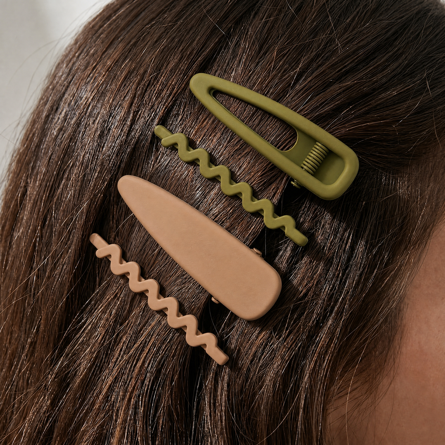Two hair clips, one green and one beige, on a person's hair.