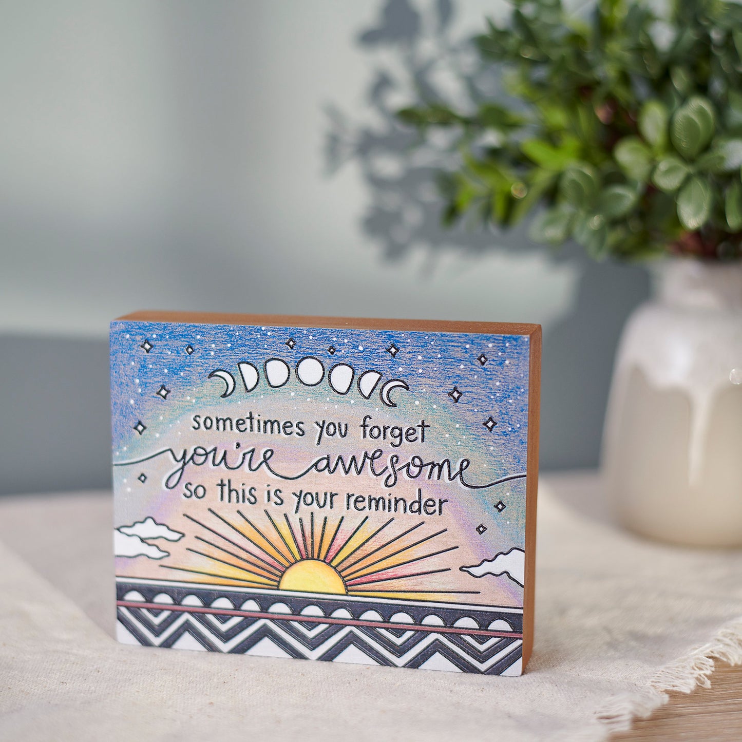 Box sign with motivational quote on a surface with a plant in the background