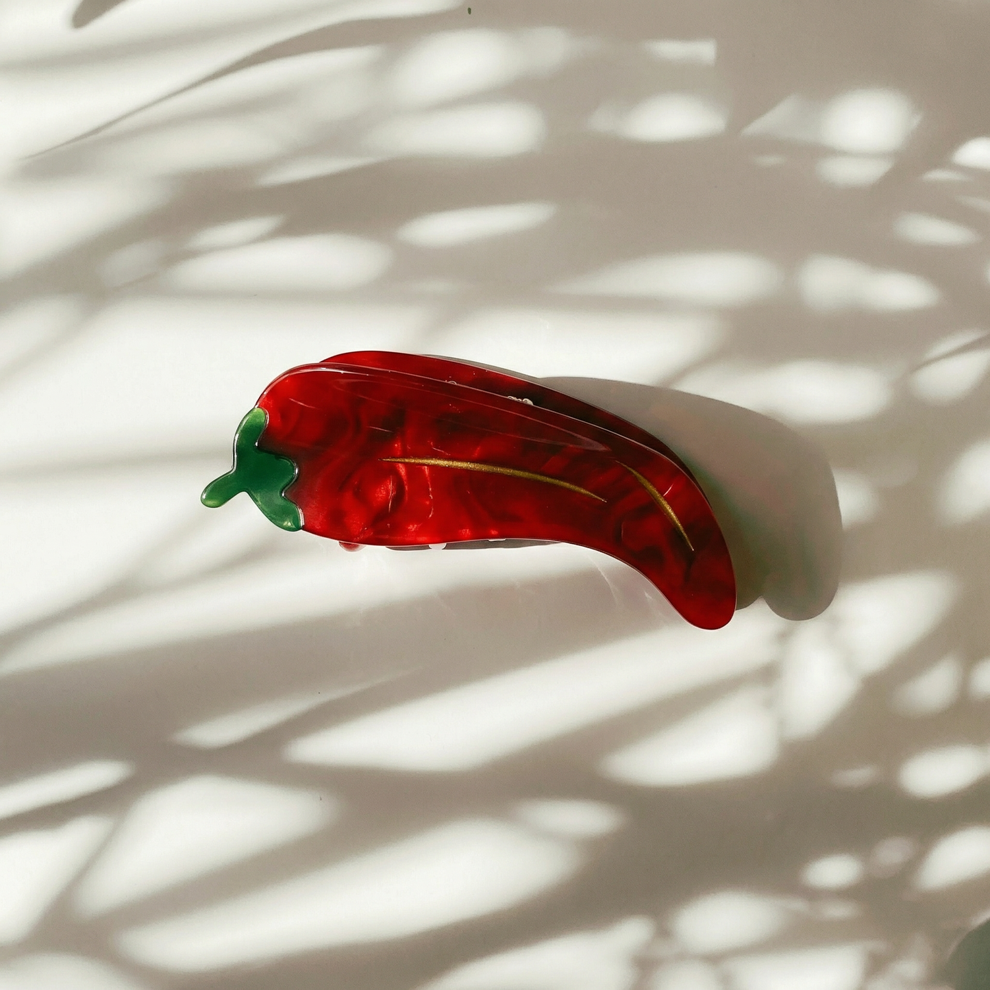 Red and green hair clip on a white surface with shadows