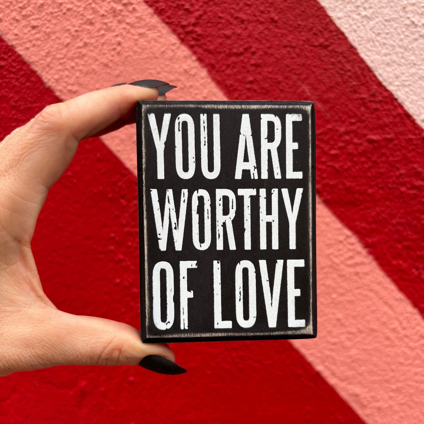 Hand holding a sign with 'You are worthy of love' text against a red background