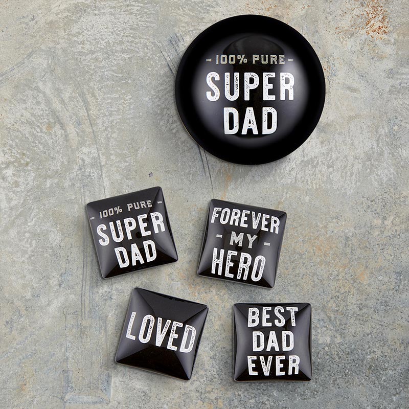 Set of black magnets and one round paperweight with white text about dads on a stone surface
