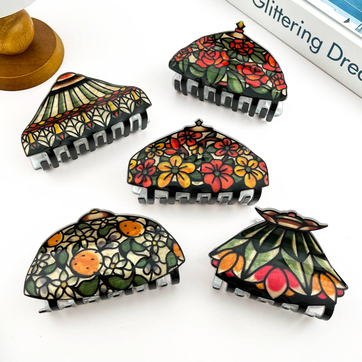Five decorative claw hair clips, each featuring a different colorful floral and fruit pattern with black claw bases.