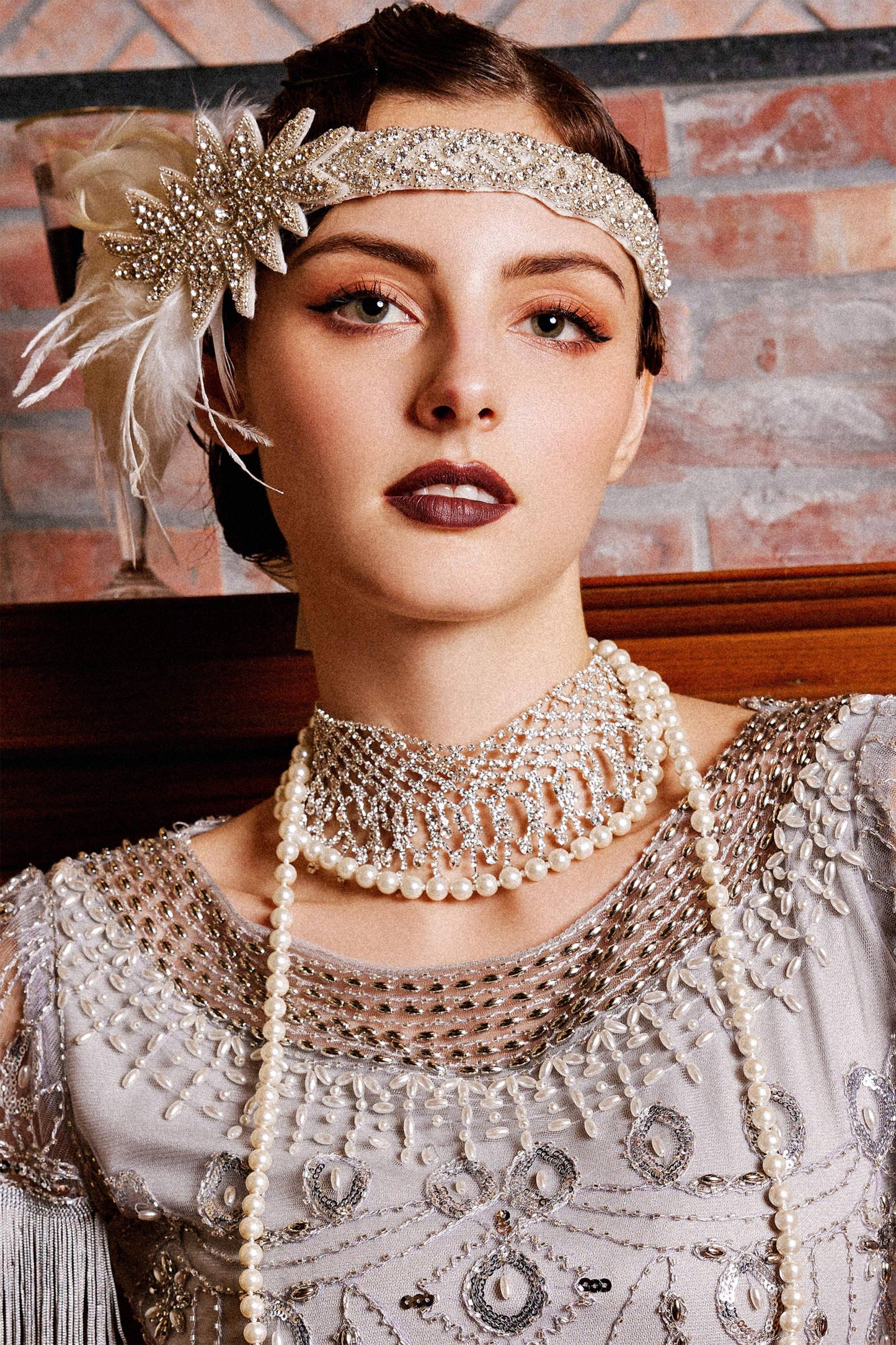 Woman wearing a vintage-style headband and pearl necklace against a brick wall.