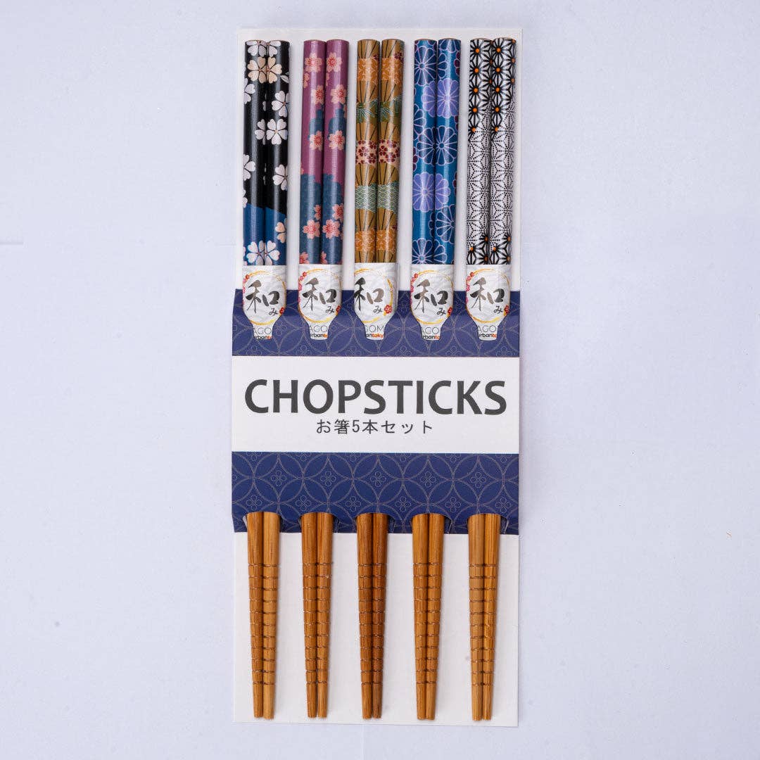 A set of five Japanese chopsticks in a white and navy cardboard holder, featuring various traditional patterns on the handles and light brown bamboo-style tips.