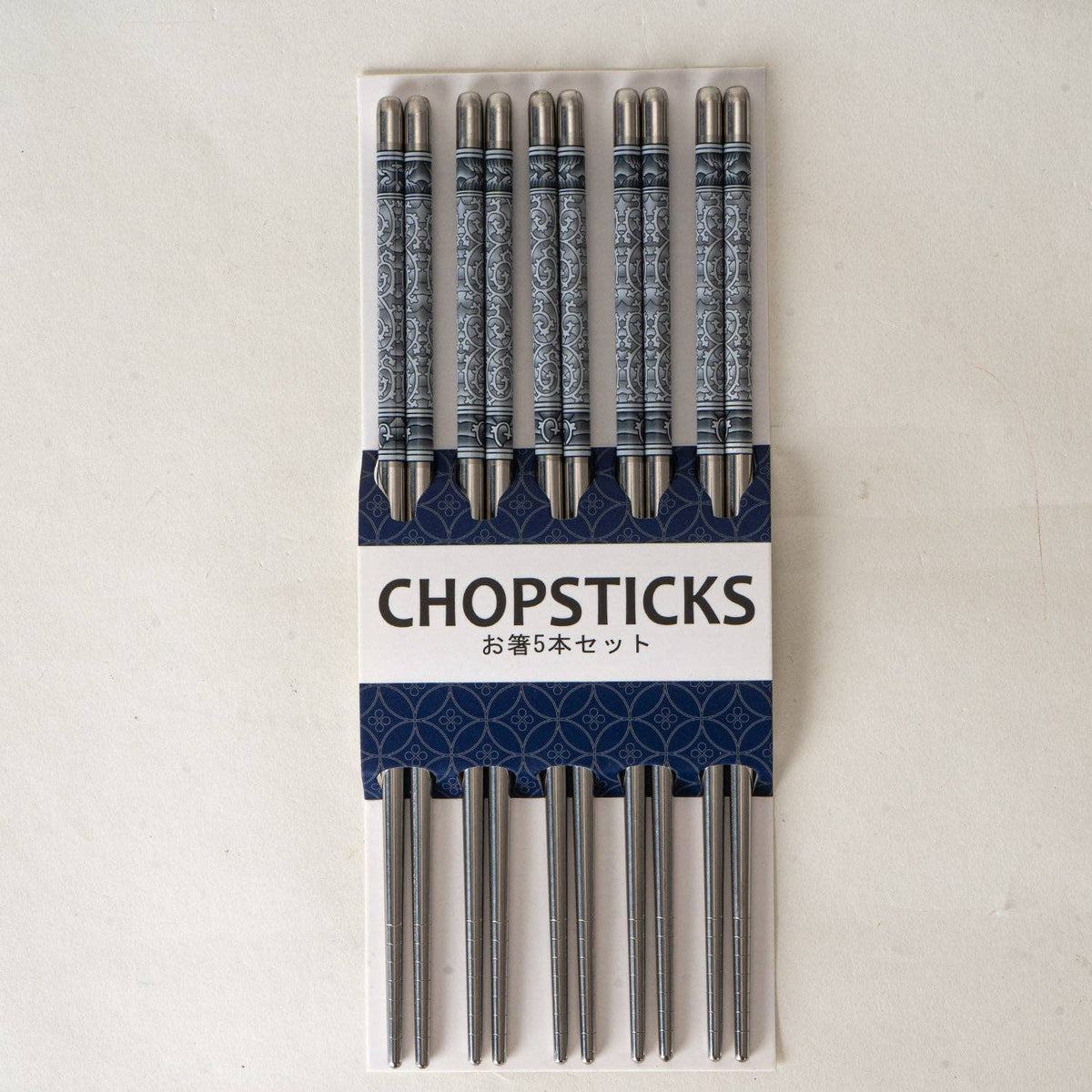 A set of five decorative stainless steel chopsticks in a white and navy blue cardboard package