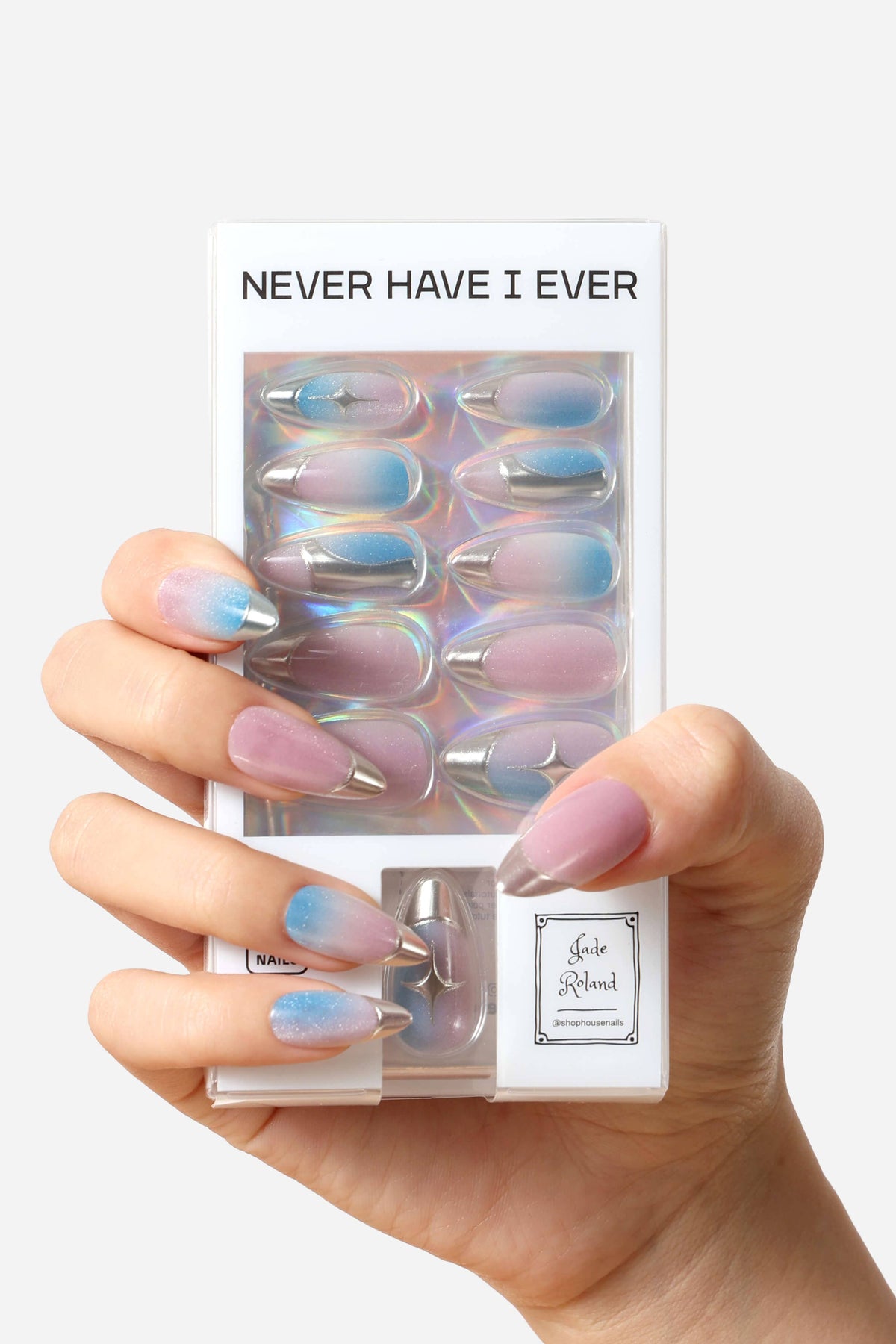 A hand holding a package of false press-on nails. The nails have a pastel gradient design transitioning from lavender-pink to light blue, with a metallic silver glitter accent at the tips.