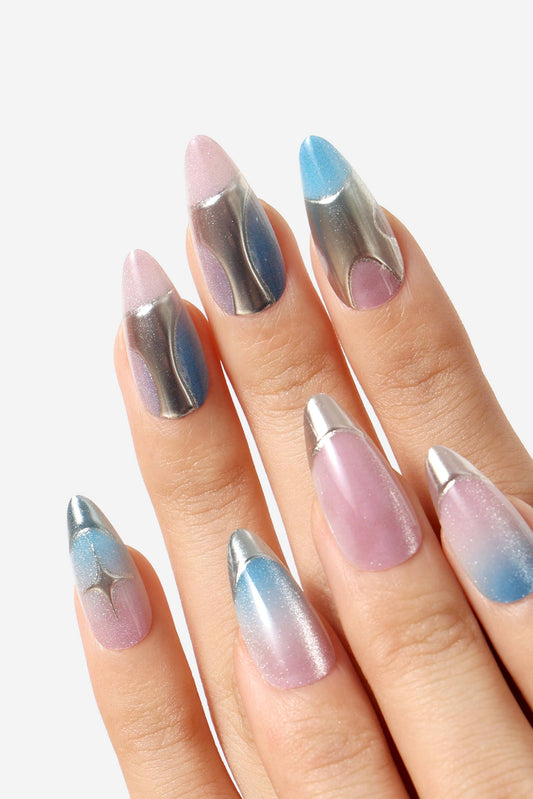 A close-up of a hand with long stiletto-shaped nails painted in a pastel gradient design. The nails feature a mix of metallic silver, light pink, lavender, blue, and white gradient patterns, with metallic silver tips.