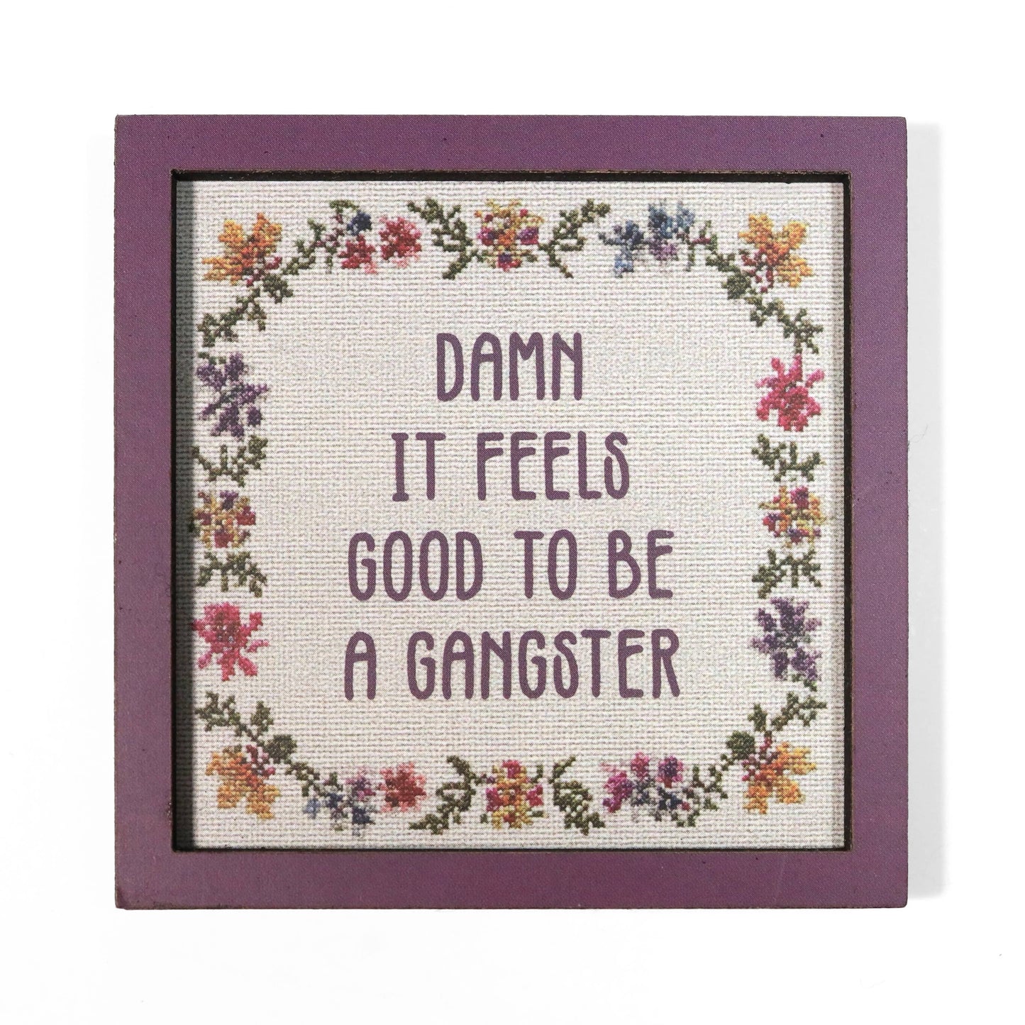 Cross stitch style magnet with floral border and quote 'Damn it feels good to be a gangster'.