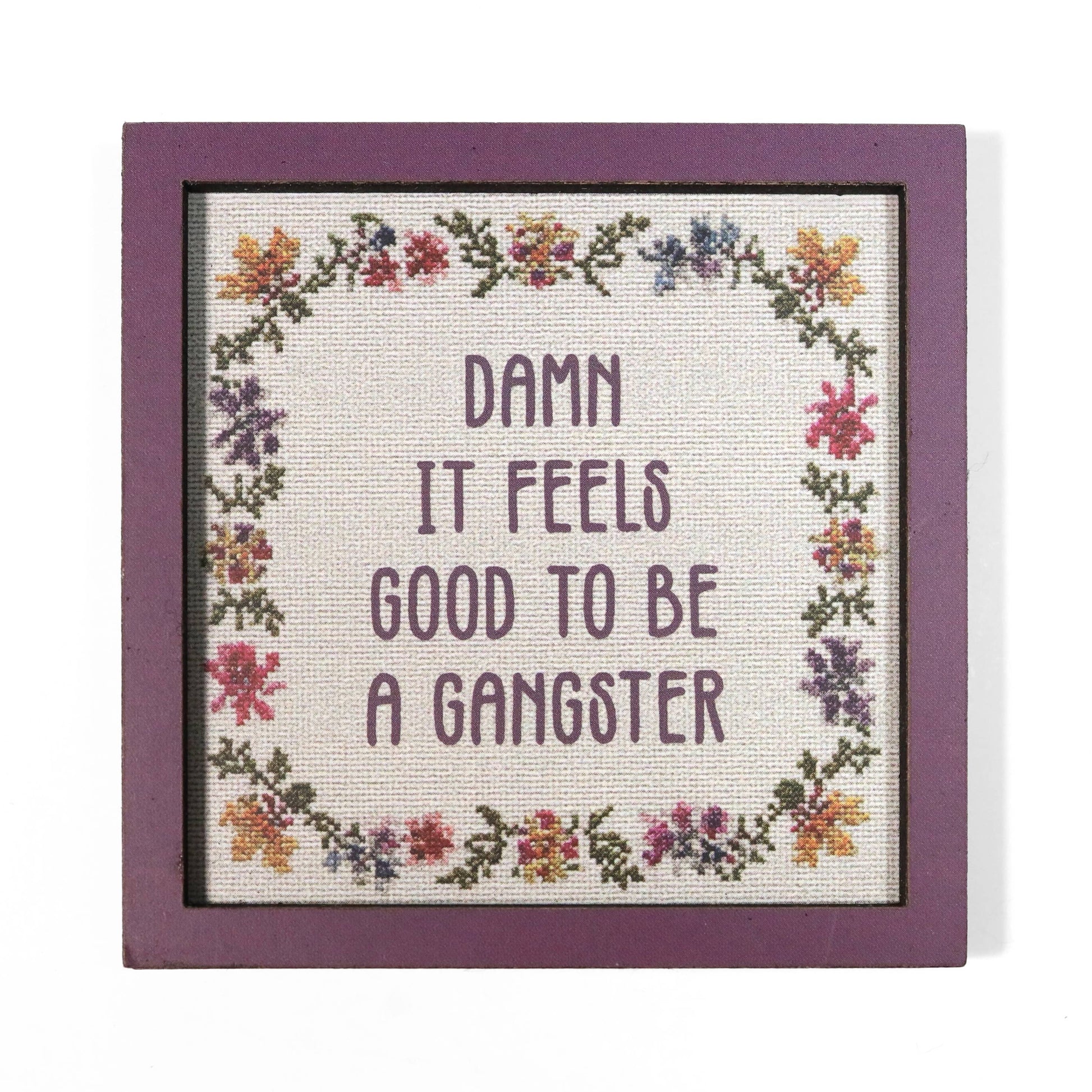 Cross stitch style magnet with floral border and quote 'Damn it feels good to be a gangster'.
