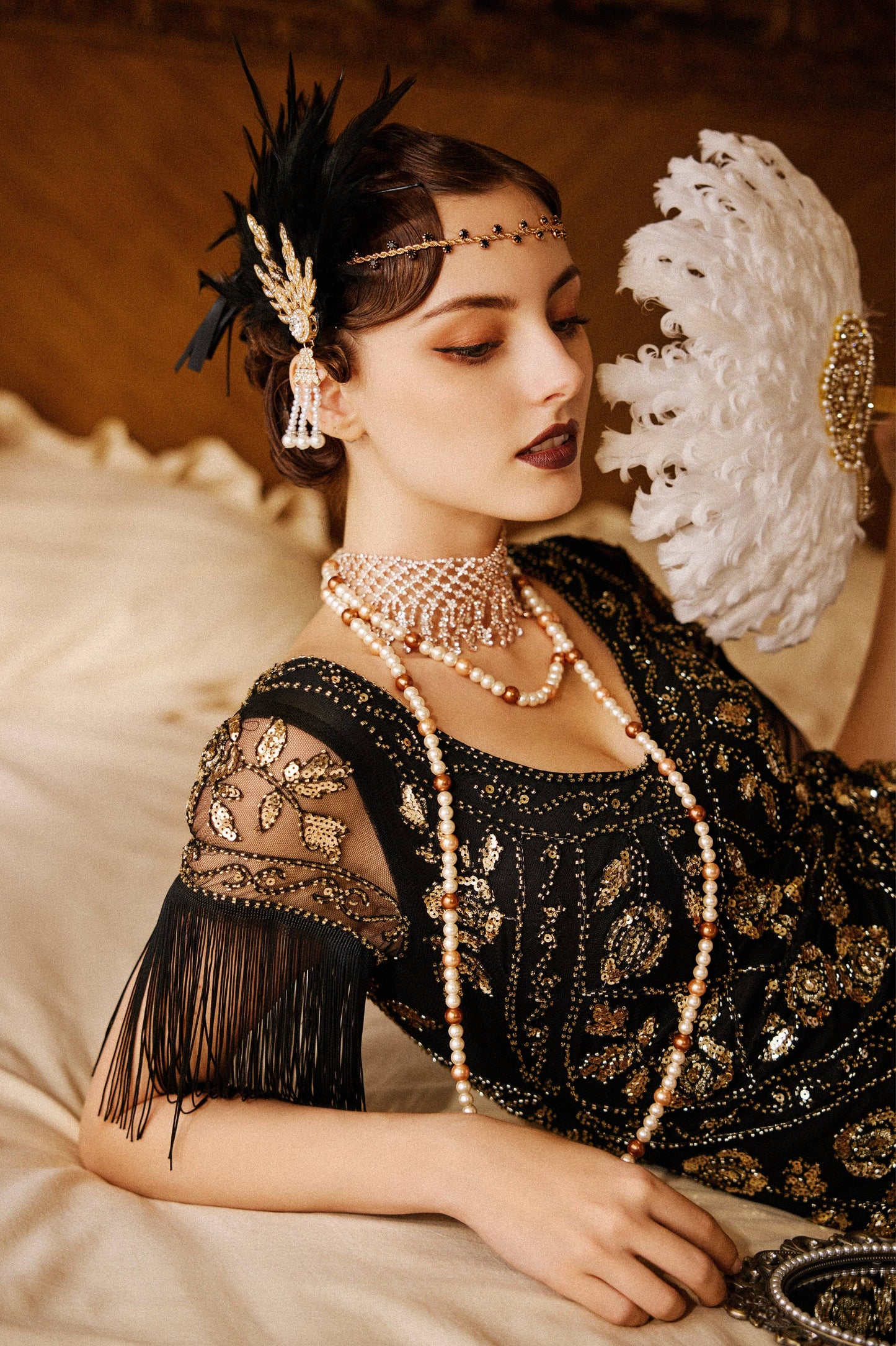Woman in a black dress with gold embellishments and jewelry, holding a decorative fan.