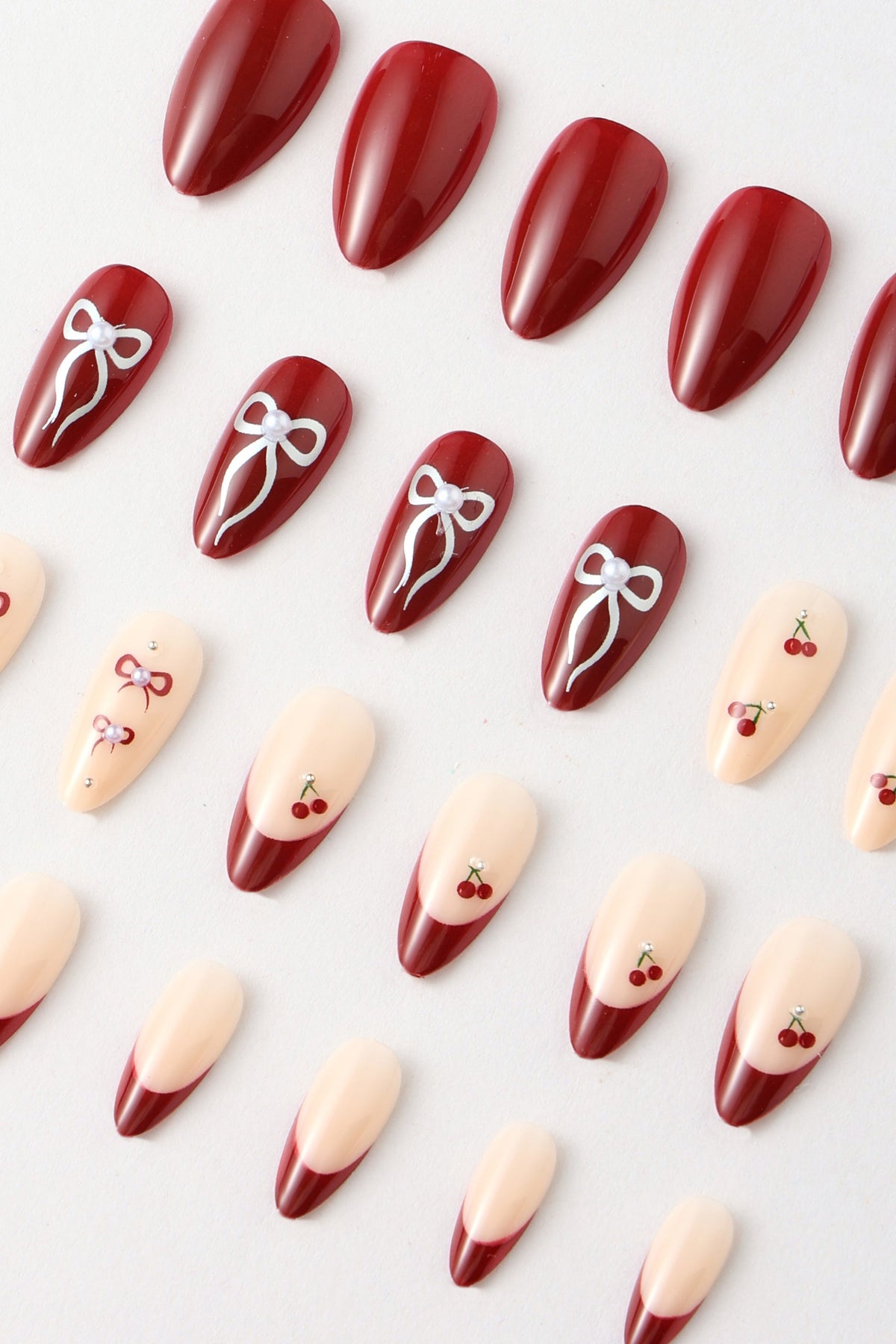 Press-on nails in deep red with cherry and bow designs
