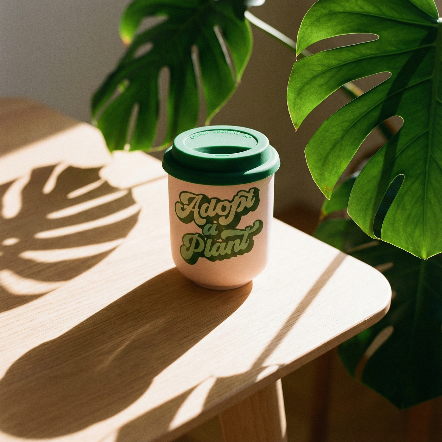 Cup with 'Adopt a Plant' text on a wooden surface with green leaves in the background