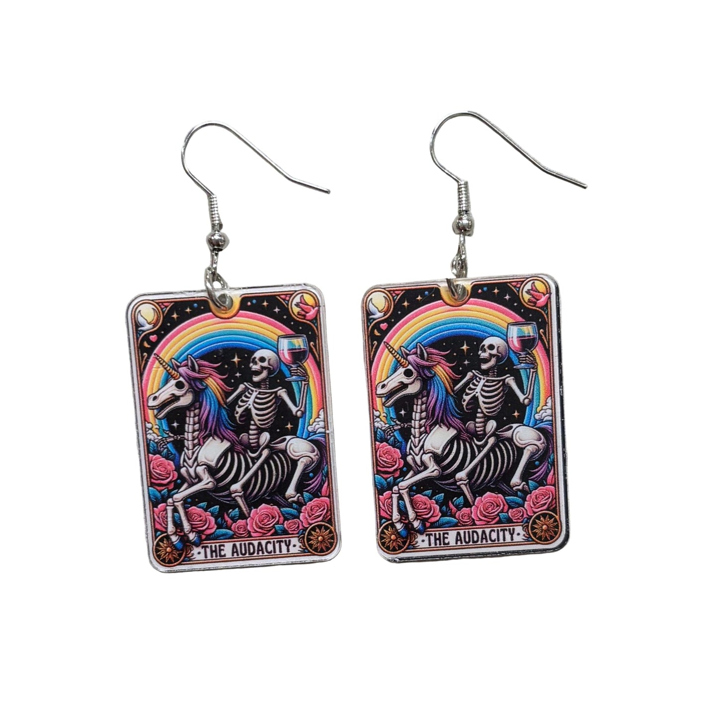 Skeletal unicorn earrings with rainbow arch and 'The Audacity' text on a textured gray background