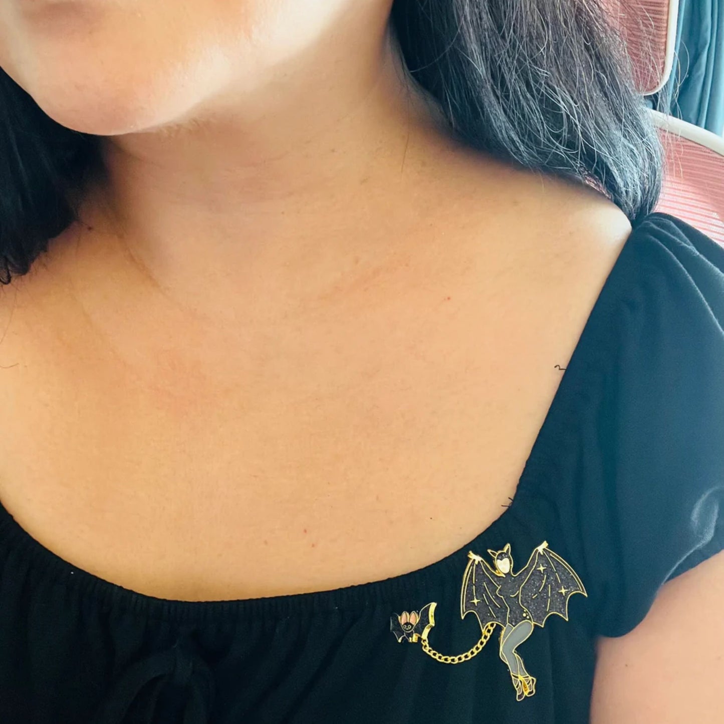 Person wearing a black top with a decorative bat enamel pin on the shoulder.