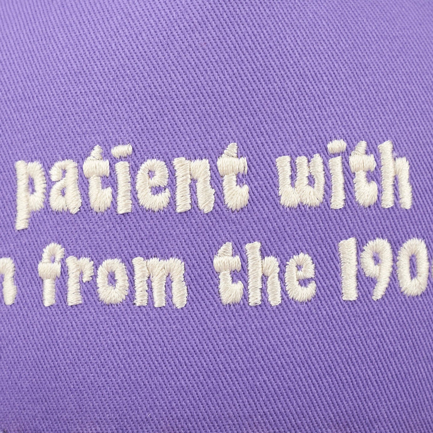 Text 'patient with' embroidered on a purple fabric background