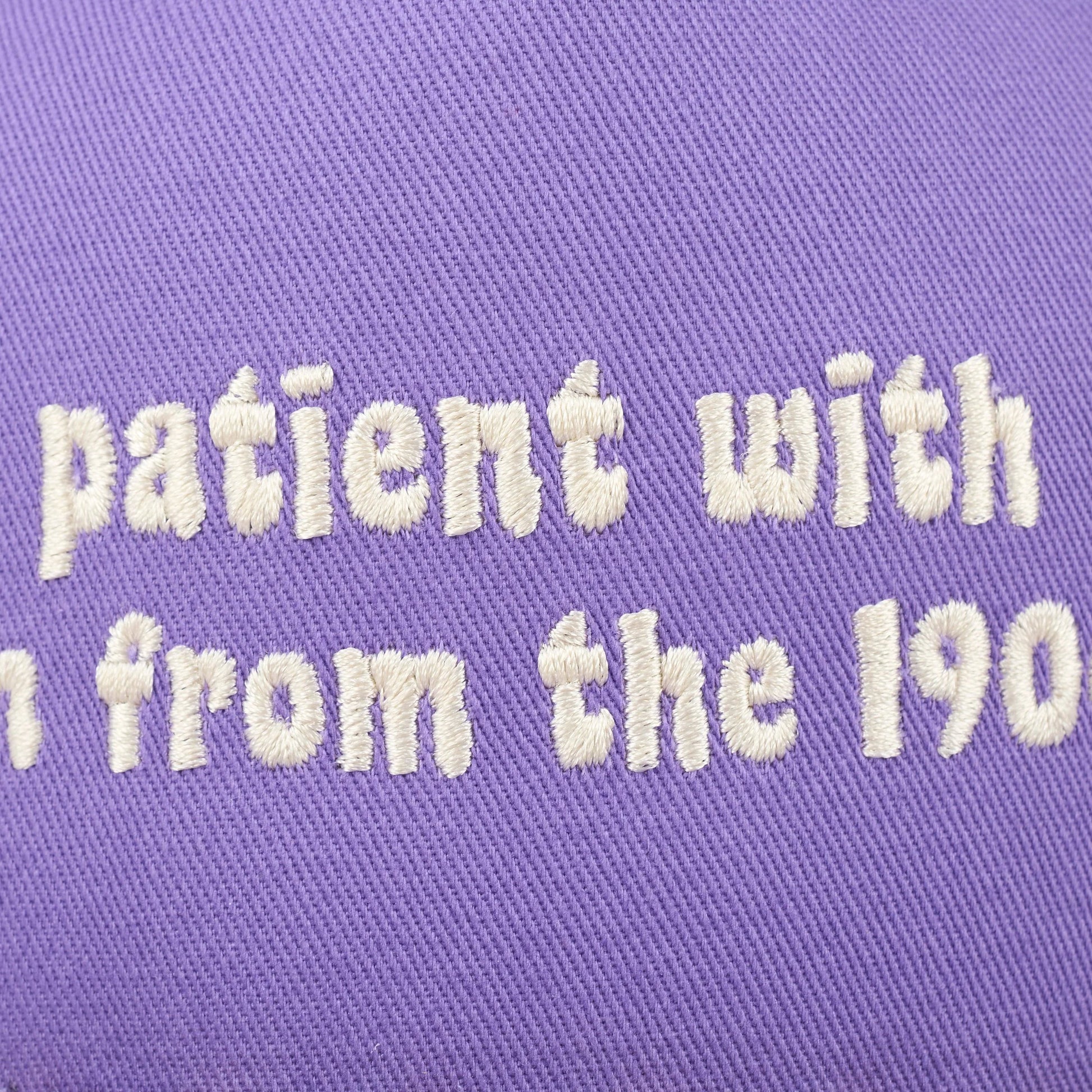 Text 'patient with' embroidered on a purple fabric background