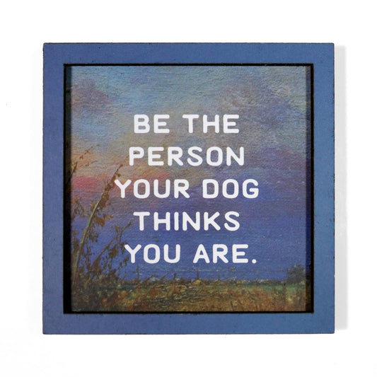 Magnet with a motivational quote 'Be the person your dog thinks you are' against a scenic background.