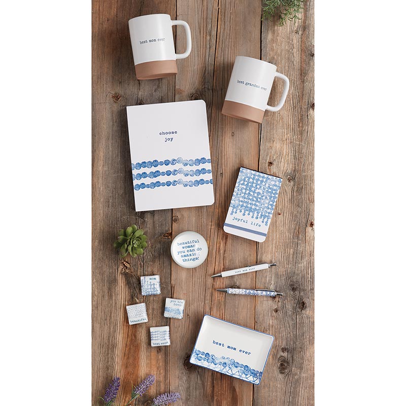 Collection of mugs, notebooks, and coasters on a wooden surface with motivational phrases.