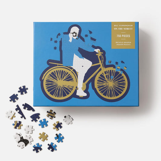 Jigsaw puzzle box with bicycle-themed design and scattered pieces on a white background