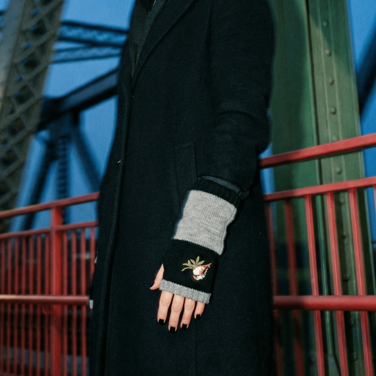 Woman in a black coat and gloves standing on a bridge at night.