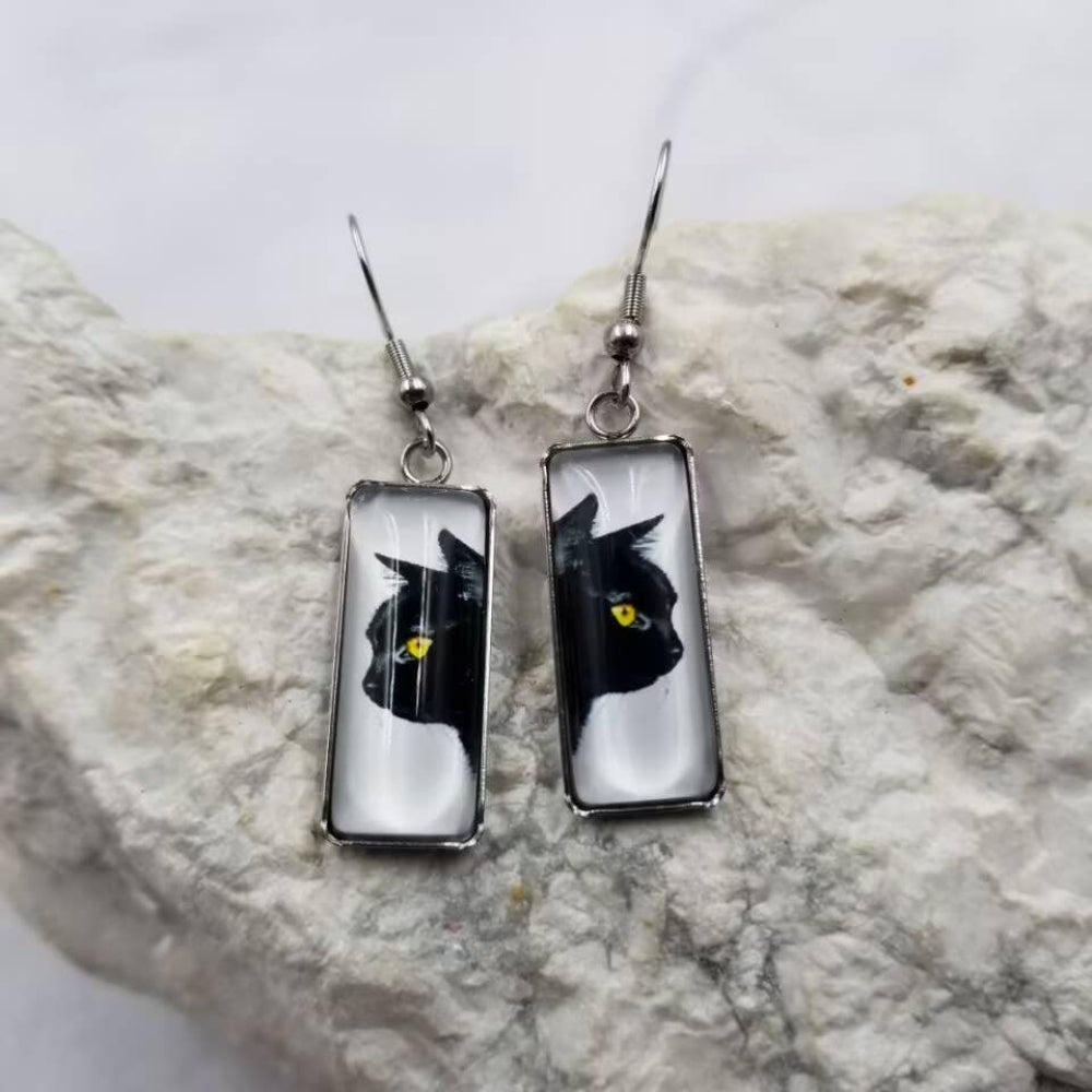 Pair of earrings with black cat design on a textured stone surface