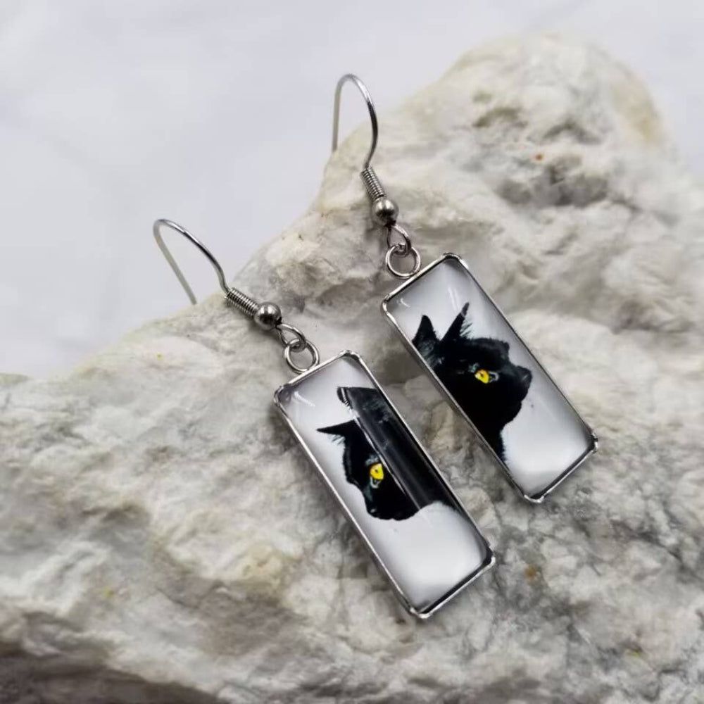 Rectangular earrings with black cat designs on a stone surface