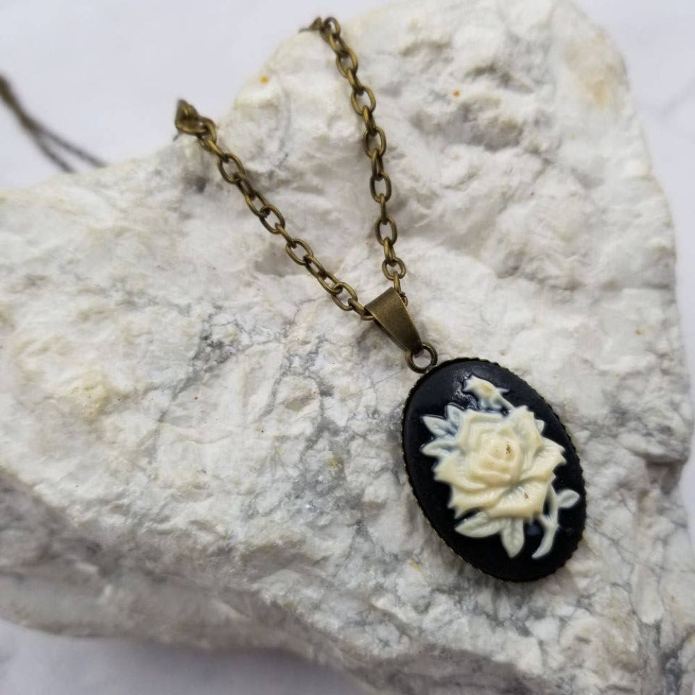 Necklace with a black pendant featuring a white rose design on a marble surface