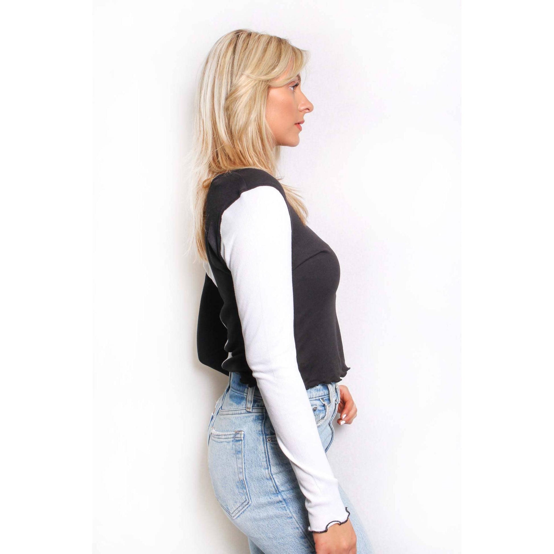Woman wearing a black and white spliced long-sleeve shirt and blue jeans on a white background