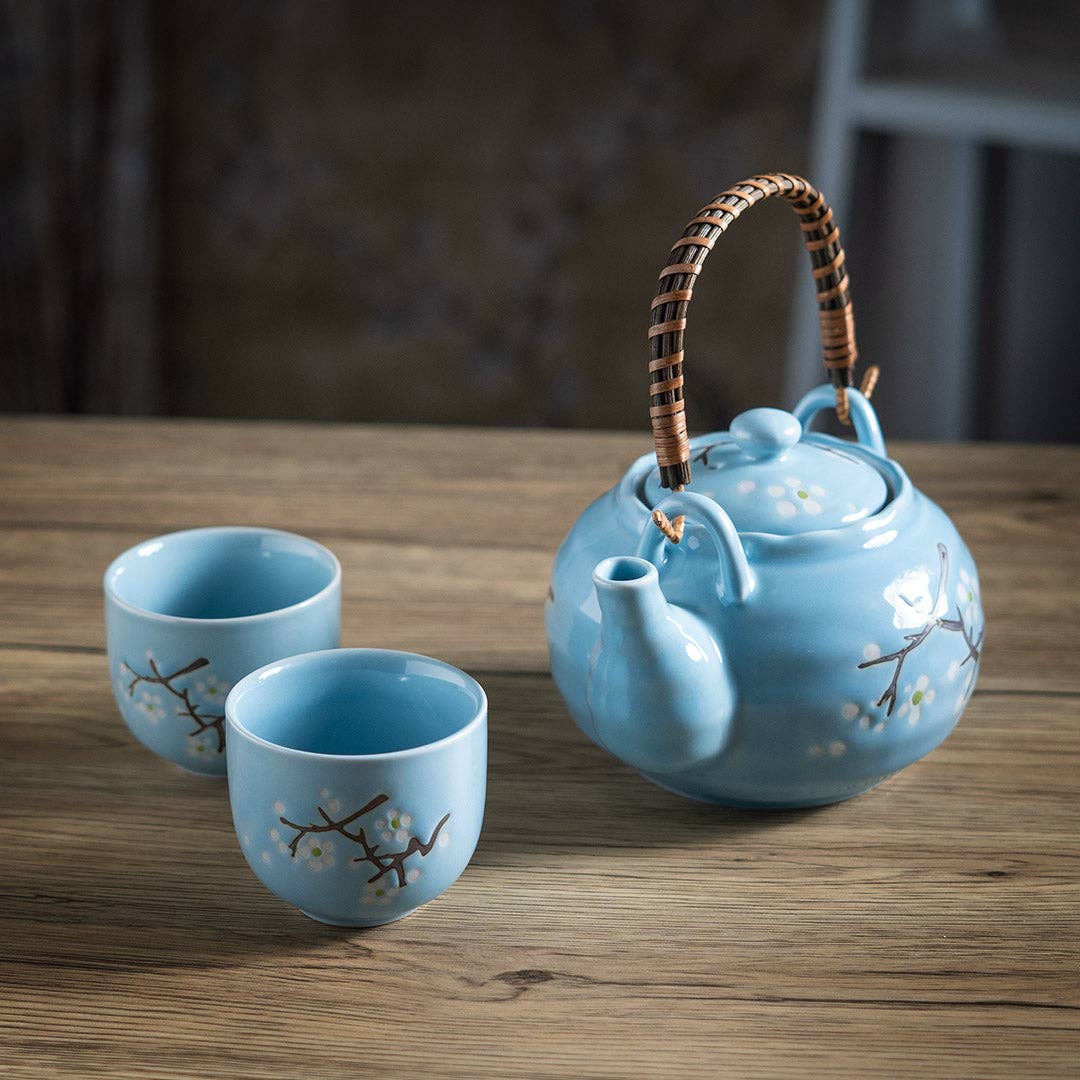 Blue ceramic teapot and two cups with floral designs on a wooden table.