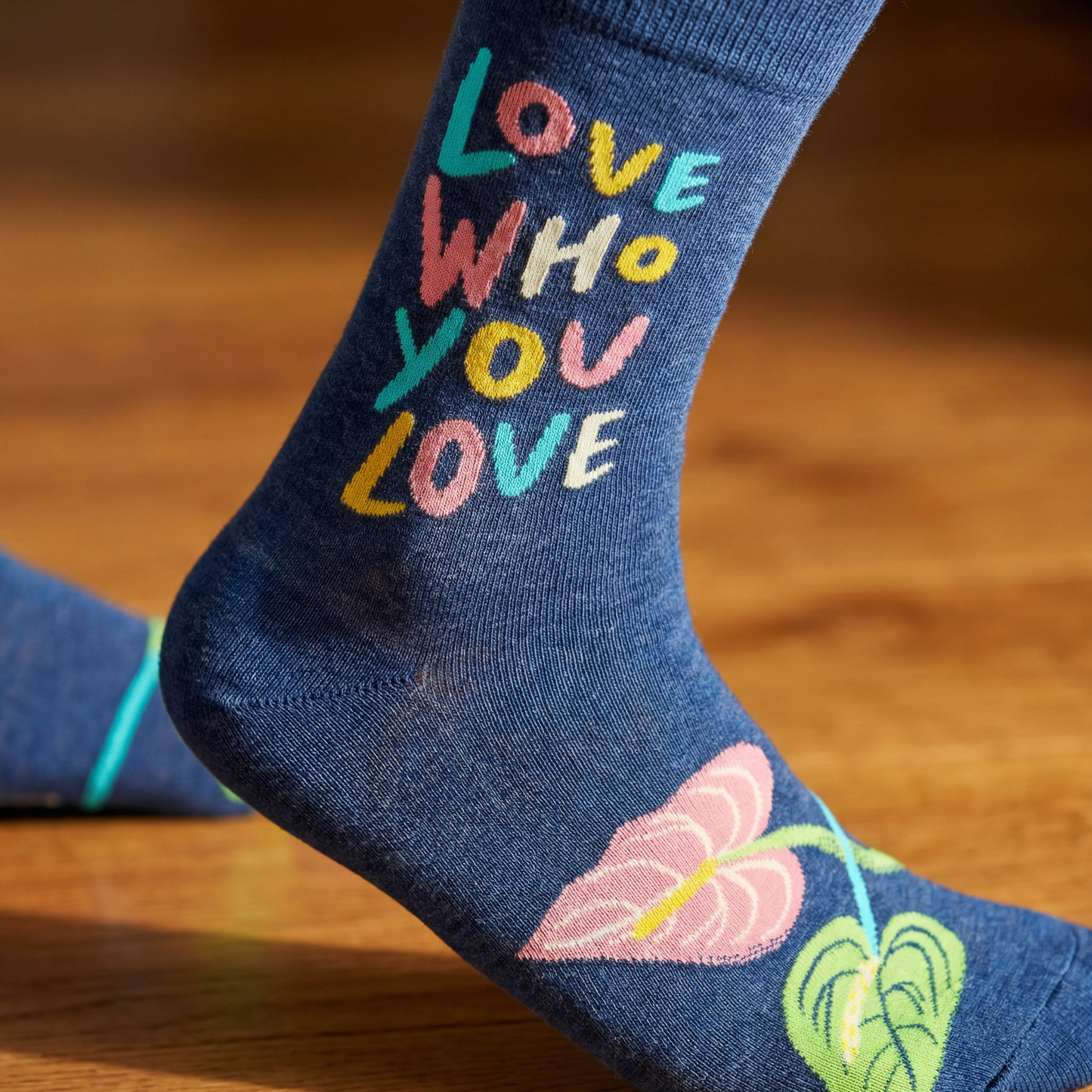 Blue sock with colorful text and leaf design on a wooden surface