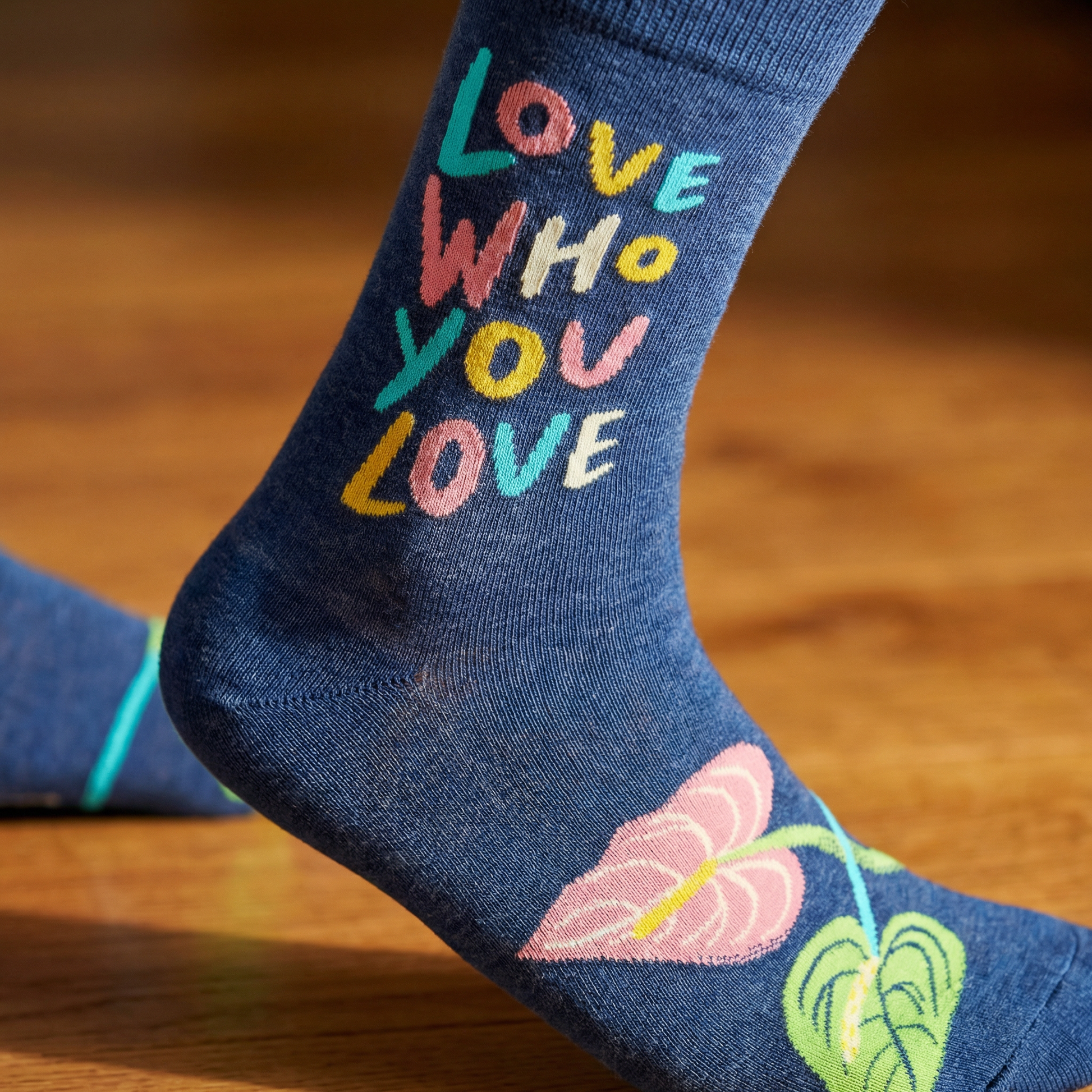 Blue sock with colorful text and leaf design on a wooden surface