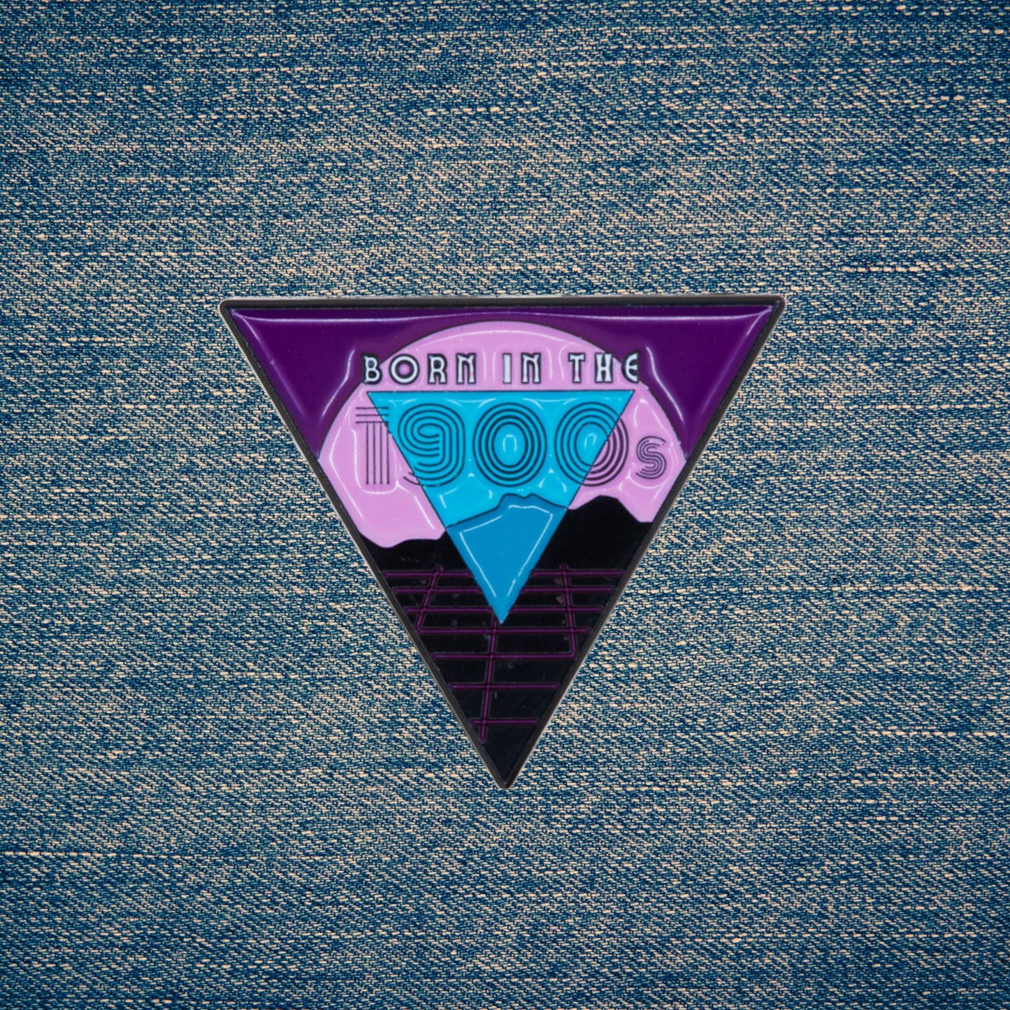 Triangular enamel pin with 'Born in the 1900s' design on a denim background