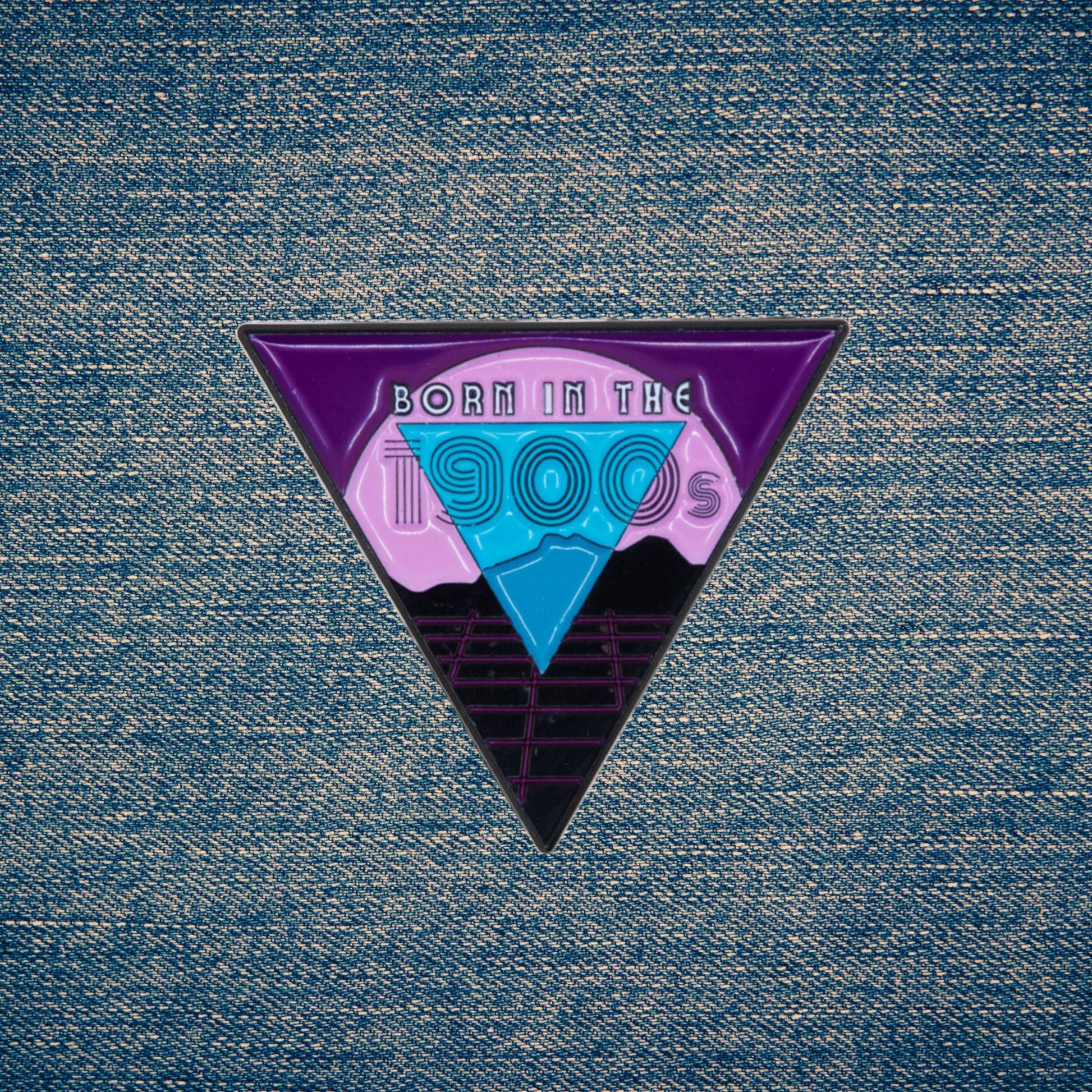 Triangular enamel pin with 'Born in the 1900s' design on a denim background