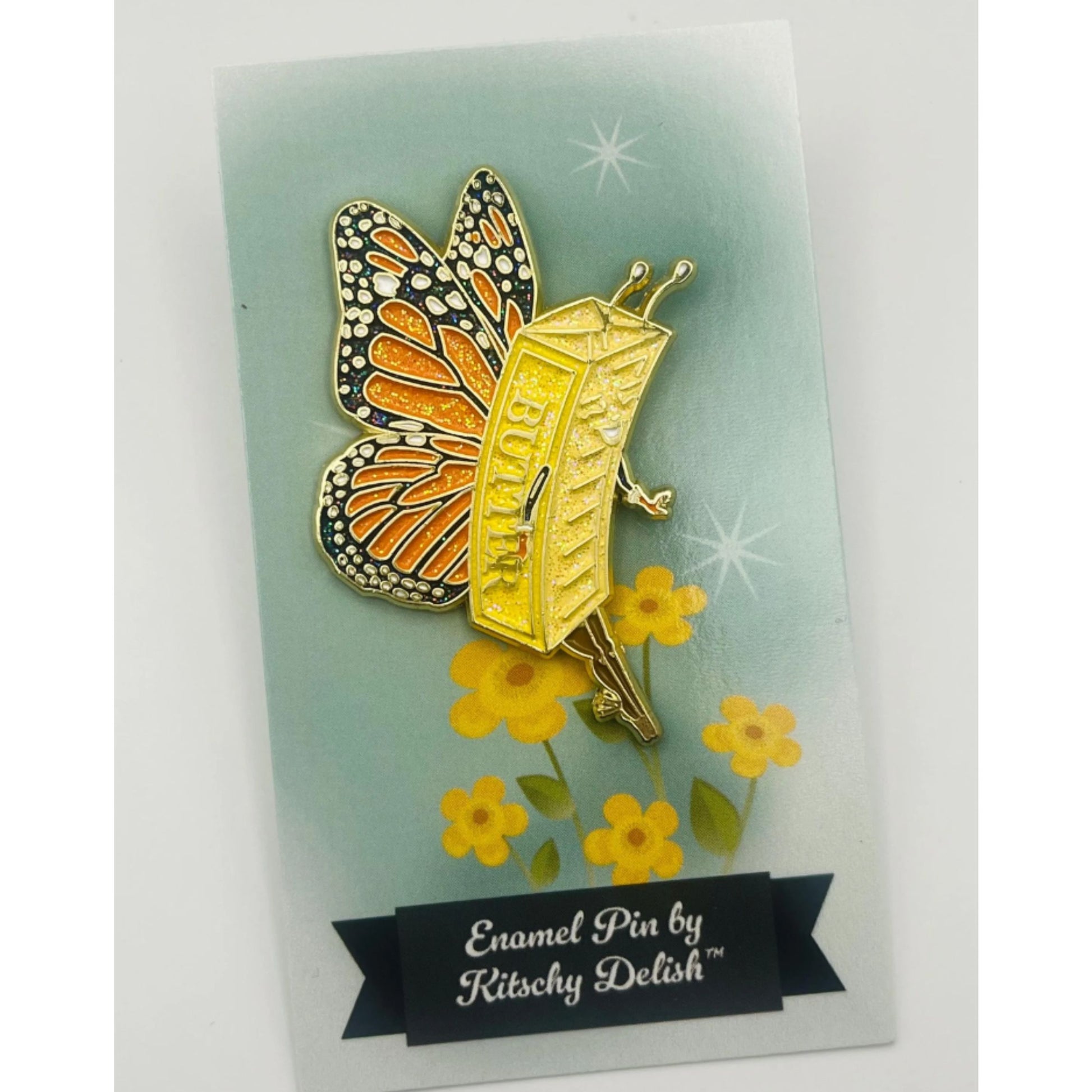 Butterfly-shaped enamel pin on a card with yellow flowers and 'Kitschy Delish' branding.