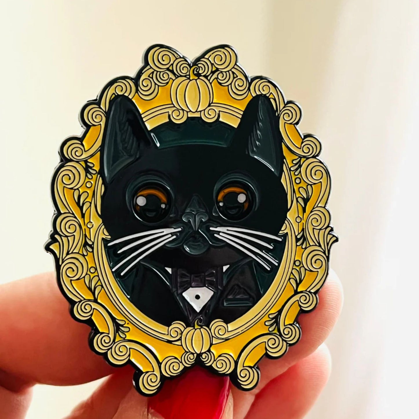 Black cat enamel pin with a gold frame held by a hand