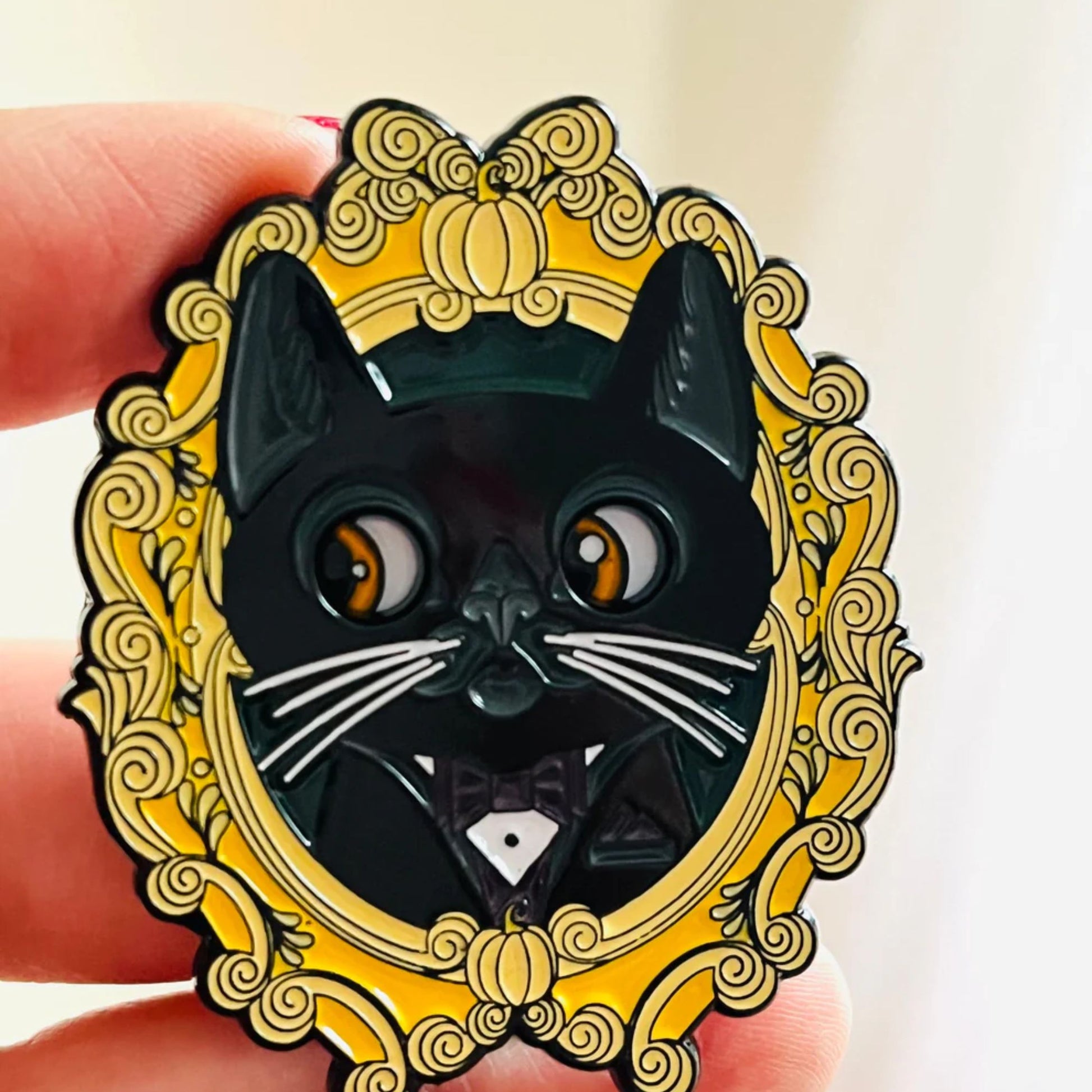 Black cat enamel pin with gold decorative frame held by a hand