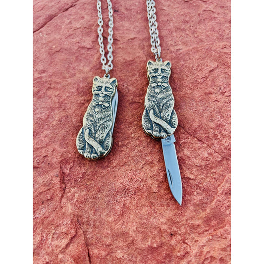 Two silver cat-shaped switchblade necklaces with cut-out designs on a pink stone background