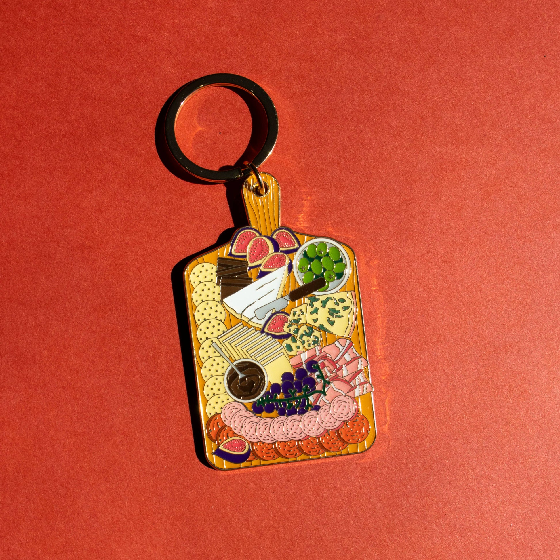 Keychain shaped like a charcuterie board with food items on a red background