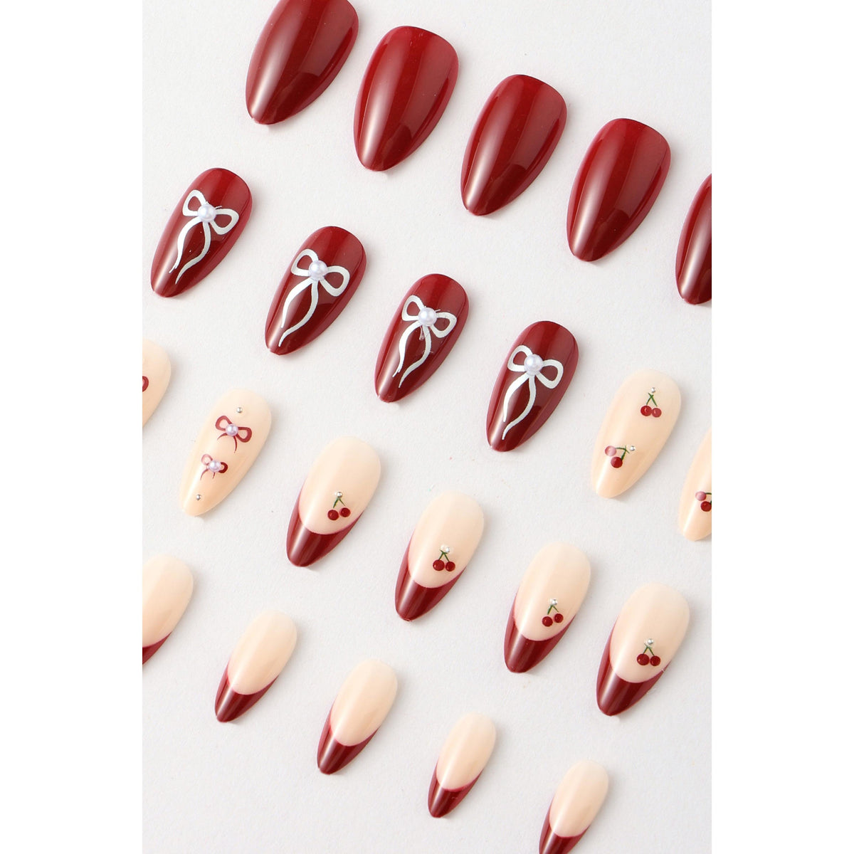 Press-on nails in deep red with cherry and bow designs
