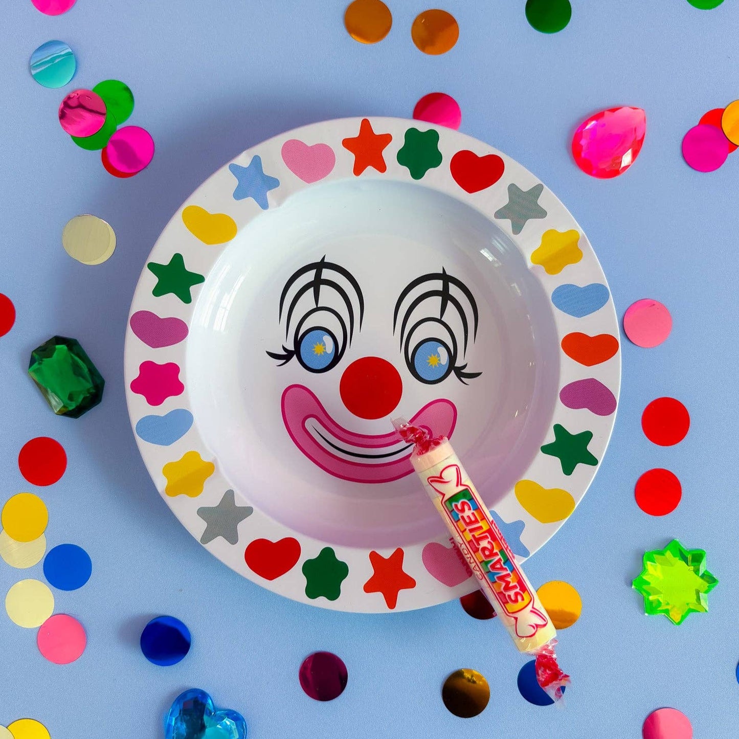 Colorful clown face plate with candy on a blue background with confetti