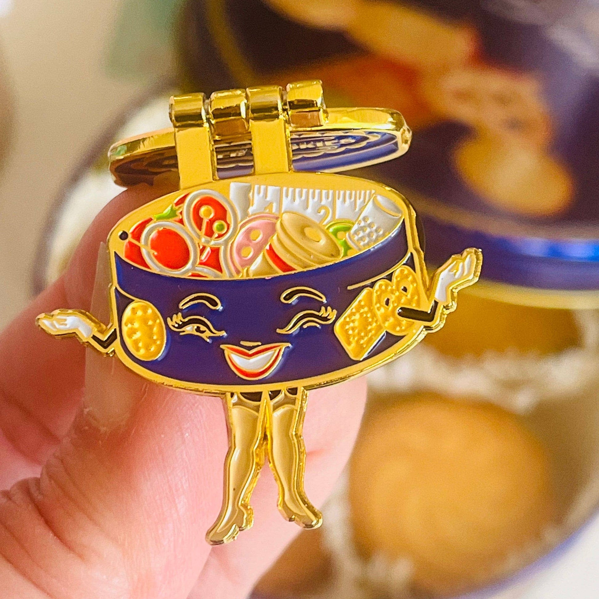 Colorful enamel pin of a smiling food container held by a hand