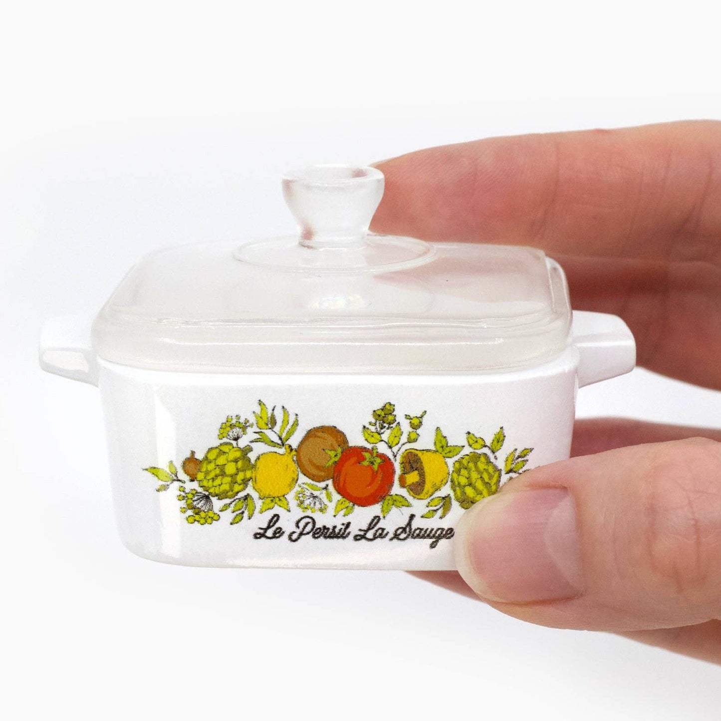 Small white container with fruit design and 'Le Persit La Sauge' text held by a hand on a white background