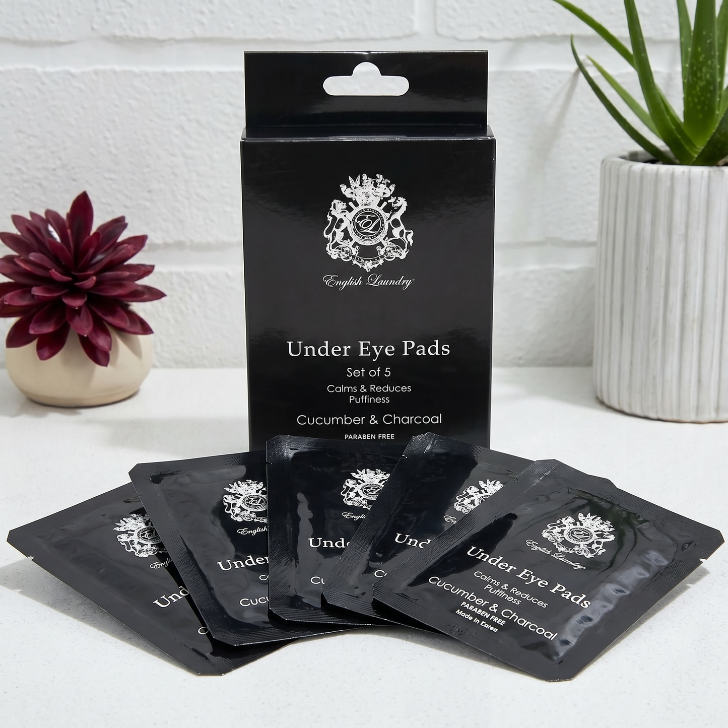 Pack of under eye pads with packaging on a white surface with plants in the background