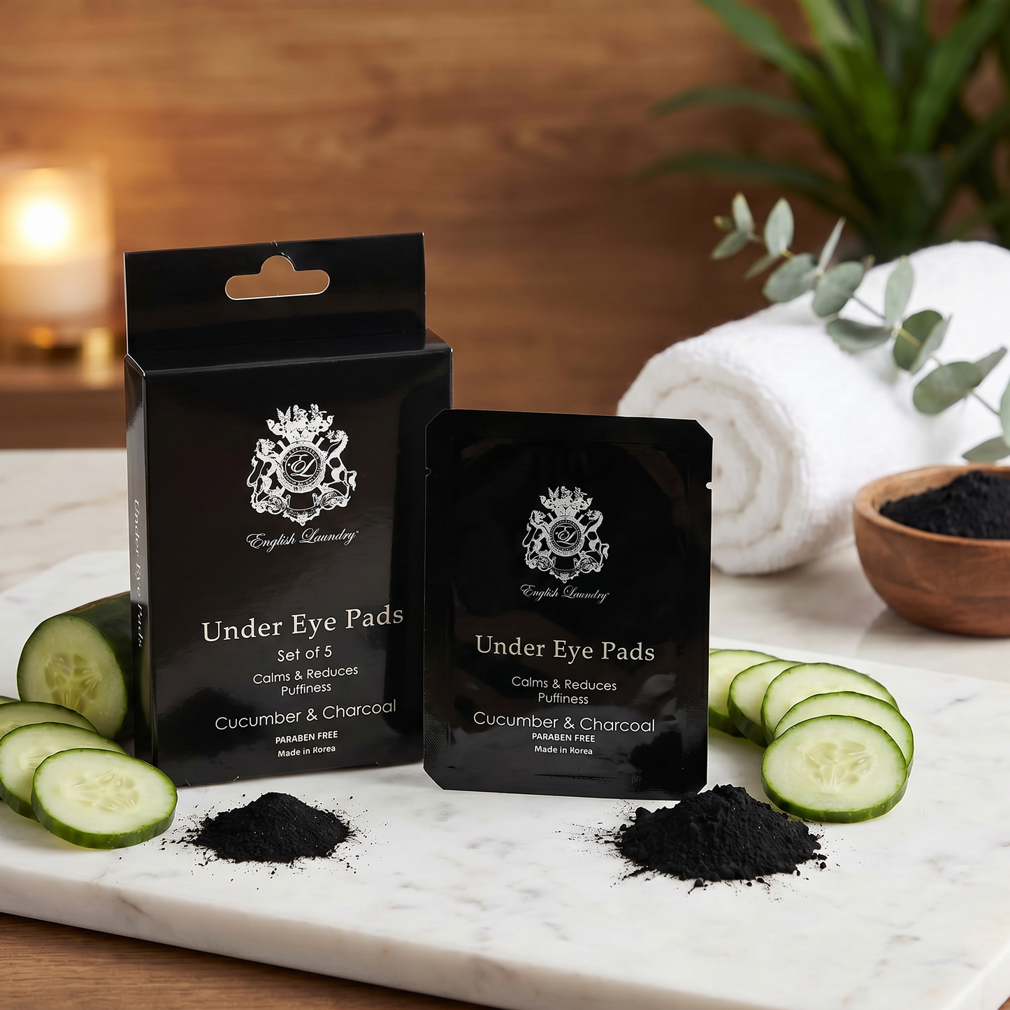 Black under eye pad packaging with cucumber slices and charcoal on a marble surface.