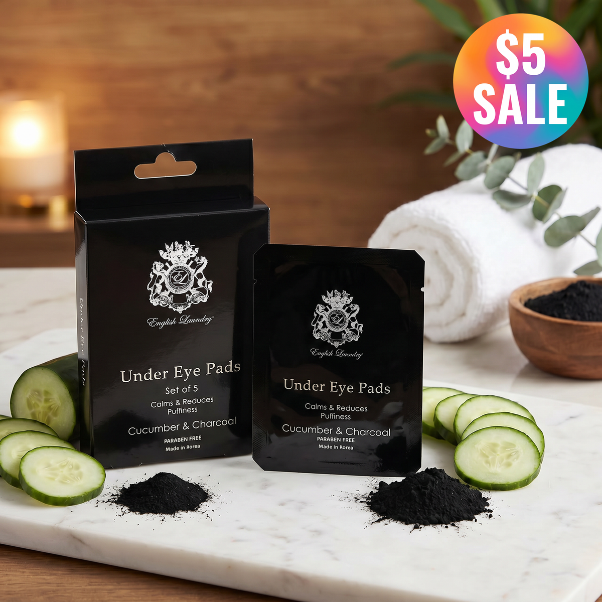 Black under eye pad packaging with cucumber slices and charcoal on a marble surface.