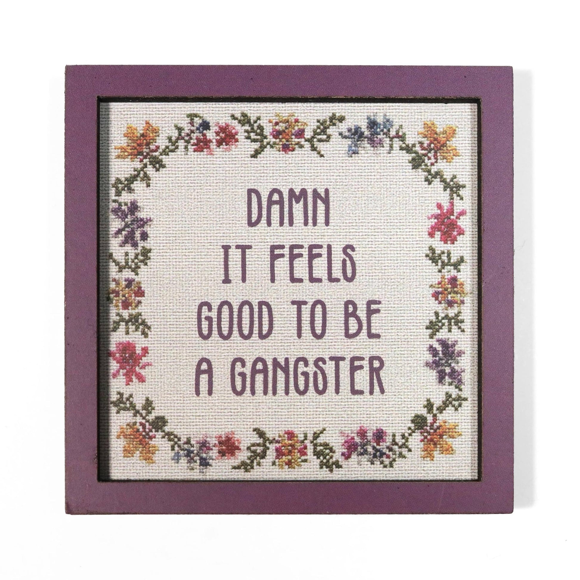 Cross stitch style magnet with floral border and quote 'Damn it feels good to be a gangster'.