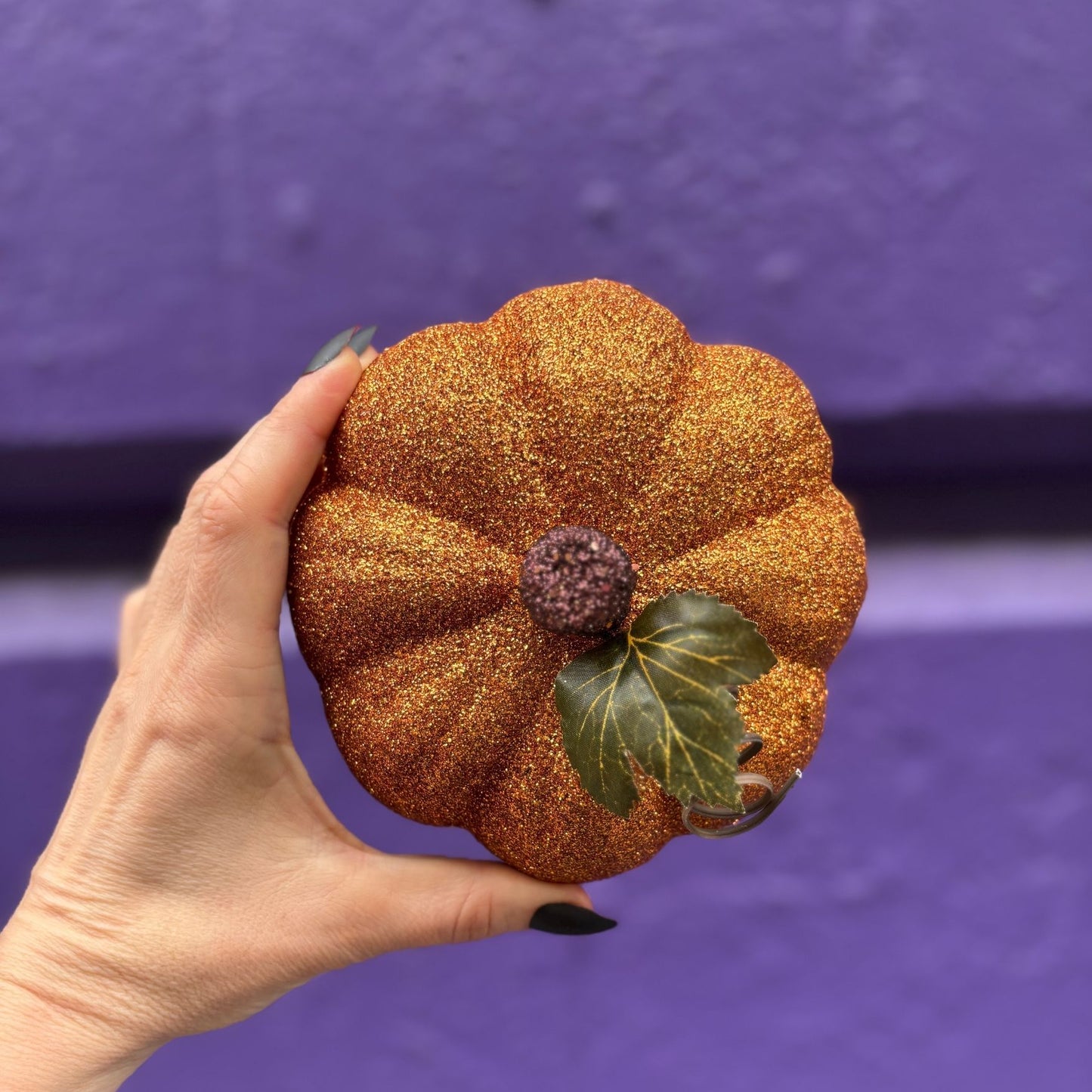 Hand holding a glittery pumpkin against a purple background