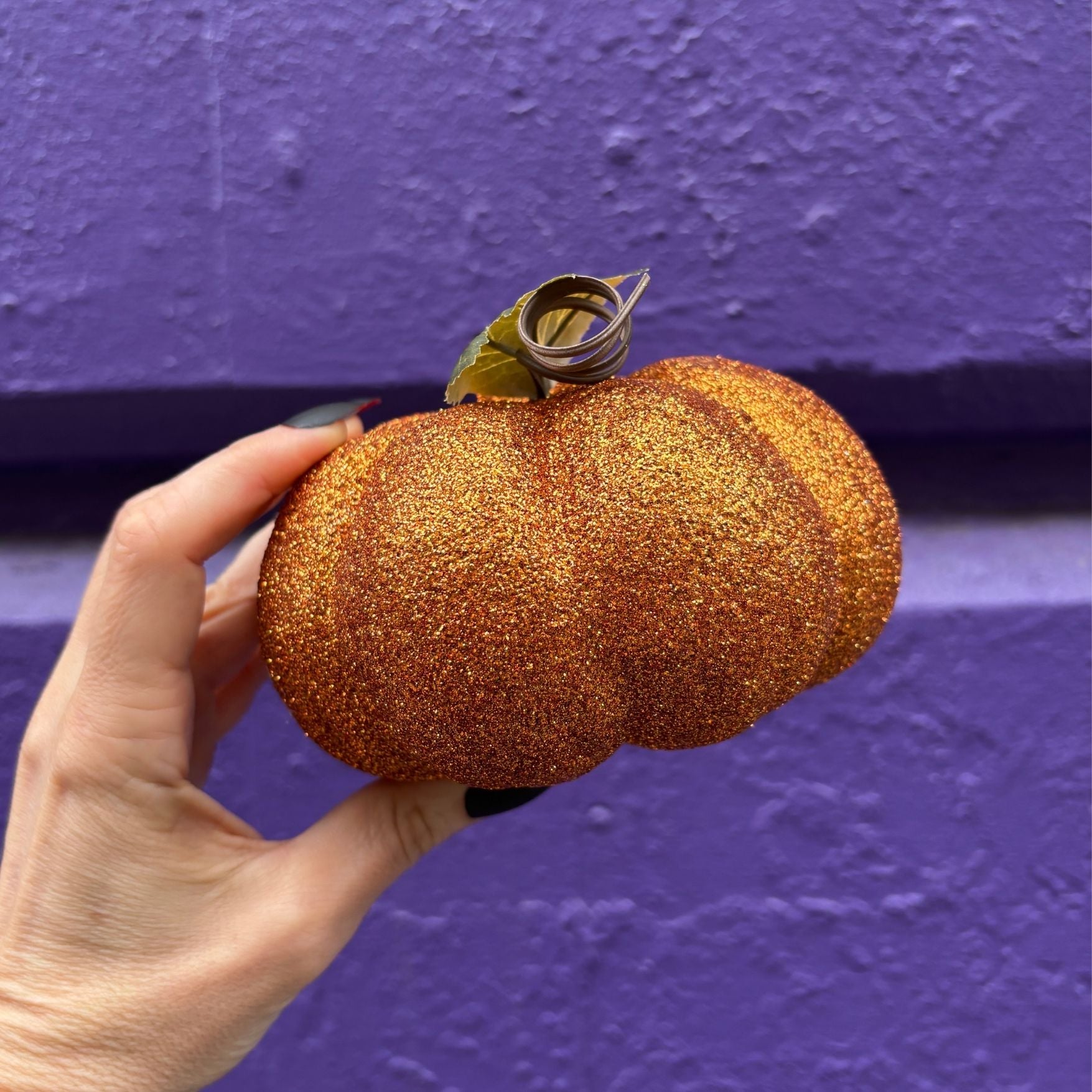 Hand holding a glittery pumpkin against a purple background